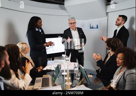 Imprenditore africano e imprenditore senior che hanno un briefing riunione in carica. colleghi che ascoltano. Foto Stock
