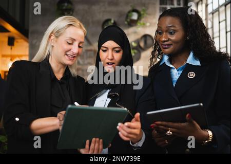 Gruppo di tre donne che utilizzano un tablet e discutono del lavoro Foto Stock