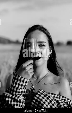 Giovane donna con bicchiere di vino rosso su campo di grano in bianco e nero Foto Stock