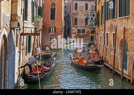 Gondolieri in gondole tradizionali che prendono i turisti in giro turistico lungo i canali stretti a Venezia, Veneto, Italia nordorientale Foto Stock