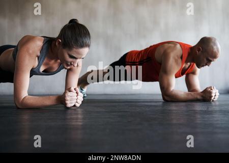 Spingi la tua strada verso il fitness. Shot di un uomo e di una donna che fanno esercizi di asse in palestra. Foto Stock