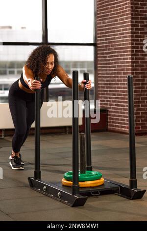 L'atleta afro-americano è impegnato in palestra. Una donna forte si allena su una slitta a croce. Motivazione sportiva e fitness. Attività ricreative sportive individuali. Foto Stock