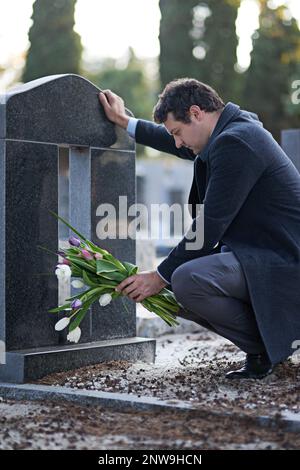 Erano i suoi fiori preferiti. Scatto di un giovane che visita un cimitero con un mazzo di fiori. Foto Stock