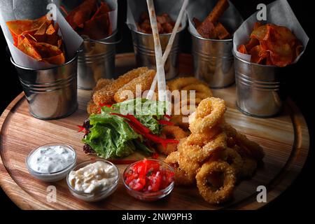 spuntini alla birra. patatine, anelli di calamari, crostini e pepite, con salse, su un asse di legno Foto Stock