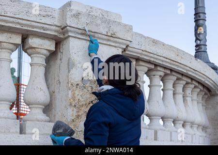 Napoli, Italia - 13 febbraio 2023: Operatore tecnico del restauro del patrimonio culturale ripara una balaustra marmorea riempiendo i fori del Foto Stock