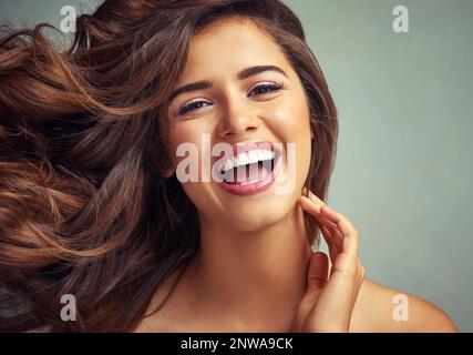 Non potrei essere più felice con i miei capelli. Ritratto studio di una bella donna con lunghe serrature in posa su uno sfondo grigio. Foto Stock