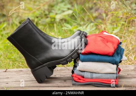 stivali neri alti da donna con suole spesse e un mucchio di cose si levano in piedi su un asse di legno al sole sulla strada, scarpe da donna e abiti invernali, fas Foto Stock