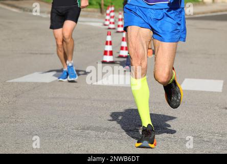 corridore anziano con la pelle della coscia che vibra durante la corsa in città sulle strade Foto Stock