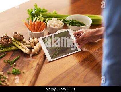 Le ricette non sono cartacee. Scatto corto di un uomo usando un tablet digitale mentre prepara un pasto sano a casa. Foto Stock