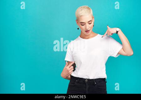 Solo in attesa delle vostre parole.... Studio girato di una giovane donna fiduciosa che punta la sua t shirt su uno sfondo turchese. Foto Stock