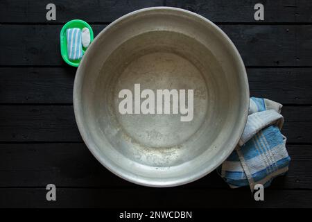 una ciotola di alluminio con acqua saponata dopo aver lavato i piedi è sul pavimento accanto al sapone e un asciugamano, una ciotola di acqua sul pavimento, lavare in una ciotola Foto Stock