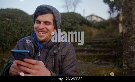 Giovane uomo in un cappello che chiacchiera al telefono e usa le app in un bellissimo paesaggio verde Foto Stock