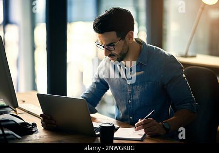 A questo tasso, inferno essere dipendente del mese. Scatto di un giovane uomo d'affari che usa un computer portatile durante una notte tarda al lavoro. Foto Stock