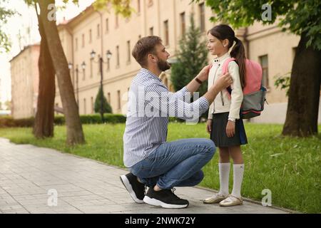 Padre aiutare la bambina a mettere in borsa scuola all'aperto Foto Stock