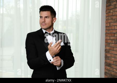 Bell'uomo elegante che si mette sul gemelli vicino alla finestra al chiuso Foto Stock