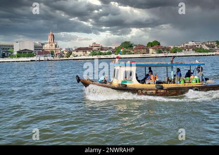 Sotto i cieli bui e inquietanti, una barca naviga lungo il fiume Chao Phraya a Bangkok, Thailandia, l'antica chiesa di Santa Cruz costruita dai portoghesi nel b/g Foto Stock