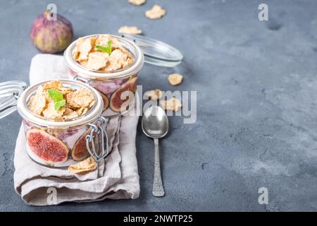 Yogurt sano fatto in casa in vaso di vetro con cereali, fichi, menta su sfondo rustico di pietra. Spazio per il testo. Colazione sana al mattino. Appena fatto Foto Stock