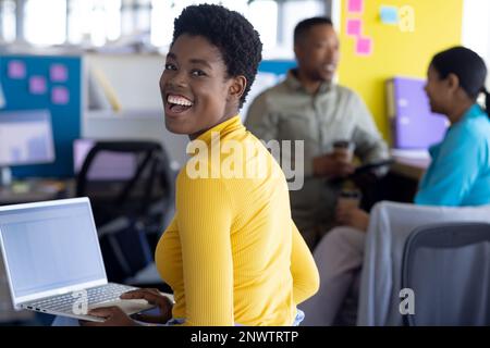 Ritratto di una donna d'affari afroamericana che usa un computer portatile e sorridente in ufficio. Lavorare in ufficio, business, finanza e concetto aziendale. Foto Stock