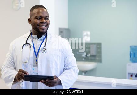 Felice medico afro-americano maschio con stetoscopio utilizzando la compressa in ospedale. Concetto di salute, ospedale e assistenza. Foto Stock
