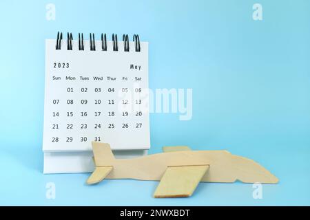 Focalizzazione selettiva del calendario da tavolo di maggio 2023 su sfondo blu con spazio copia e modello di aeroplano in legno. Concetto di viaggio e vacanza. Foto Stock