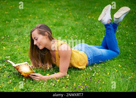 Leggere è come sognare con gli occhi aperti. una giovane donna spensierata che si rilassa in un campo d'erba con un libro. Foto Stock