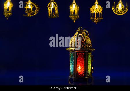 La lanterna dorata si accende su sfondo blu scuro con luci decorate per la festa musulmana del mese santo di Ramadan Kareem. Foto Stock