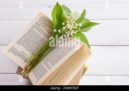 un bouquet di delicati gigli profumati della valle si trova su un libro aperto e su un tavolo di legno bianco. il concetto di buon umore, una mattina di primavera Foto Stock