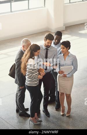 Esecuzione del piano da parte del team. Immagine ad alta angolazione di un gruppo di uomini d'affari che parlano insieme mentre si trovano in una lobby dell'ufficio. Foto Stock