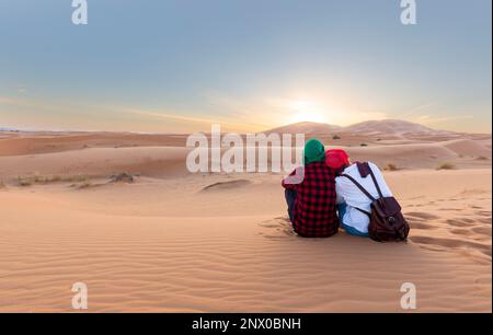 Tramonto nel deserto. Coppia romantica seduta godendo i colori caldi del deserto durante il tramonto. Deserto del marocco Foto Stock