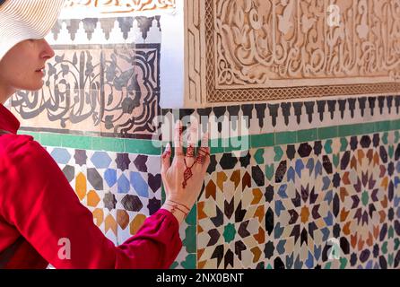 Donna in abito rosso che tocca parete in ceramica con motivo floreale a mano in henné pittura in marrakesc, marocco Foto Stock