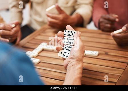 Mani, domino e amici in giochi da tavolo su un tavolo di legno per attività divertenti, legami sociali o incontri. Mano del giocatore domino che tiene un rettangolo Foto Stock