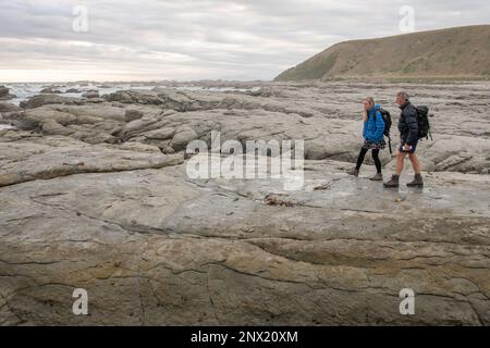 Due escursionisti camminano attraverso la costa rocciosa della penisola di Kaikoura in Aotearoa Nuova Zelanda. Foto Stock