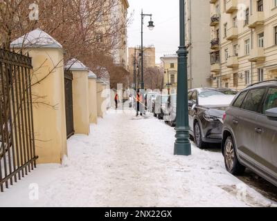 Mosca. Russia. Febbraio 25, 2023. I lavoratori delle utenze in giubbotti arancioni con pale puliscono la neve dal marciapiede su una strada cittadina in una nuvolosa giornata invernale. Foto Stock