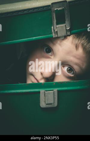 il bambino si nasconde in una vecchia valigia verde, primo piano ritratto Foto Stock