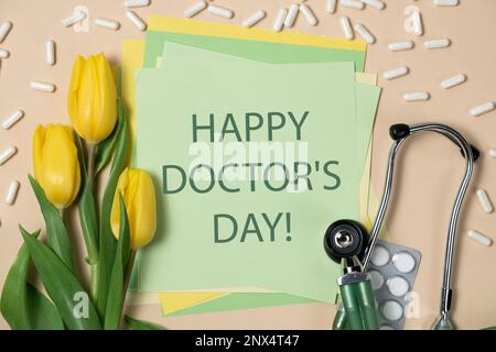 Happy Doctor's Day - cartolina con testo, stetoscopio e tulipani gialli su sfondo verde e beige Foto Stock