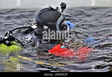 Un vigile del fuoco con la direzione dei servizi di emergenza del team di immersione del Dipartimento dei vigili del fuoco pratica uno scenario di salvataggio su ghiaccio 11 gennaio 2023, presso un lago congelato Big Sandy sul South Post a Fort McCoy, Wisconsin. Diversi vigili del fuoco con la squadra hanno preso il loro turno, indossando un vestito, reggendo un serbatoio dell'aria e una maschera a pieno facciale, e tuffandosi nelle profondità del lago Big Sandy sotto il ghiaccio sul South Post di Fort McCoy. I subacquei stavano coprendo profondità fino a 15 piedi o più completando diversi tipi di scenari di salvataggio sotto la guida di altri vigili del fuoco. I subacquei hanno preso i giri che vanno dentro e fuori dello stesso foro che è stato tagliato Foto Stock