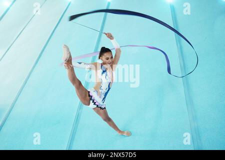 Ginnastica, donna con nastro per danza e performance, flessibilità con atleta professionista in palestra e vista dall'alto. Ginnastica ritmica, gamba in aria con Foto Stock