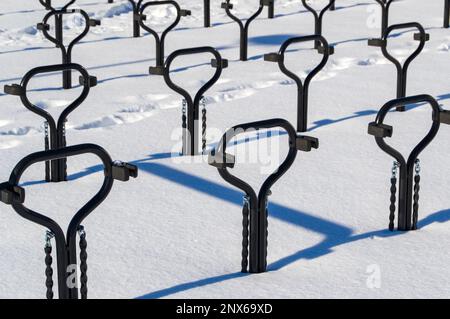 Portabiciclette in metallo nero. La foto è stata scattata in una giornata invernale di sole. Rack proietta ombre nella neve. Foto Stock