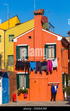 Donna che si appende lavando fuori dalle case dai colori vivaci a Burano, Venezia, Italia nel mese di febbraio Foto Stock
