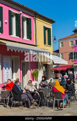 Le persone si rilassano e gustano un drink al Trexento con case dai colori vivaci a Burano, Venezia, Italia a febbraio Foto Stock