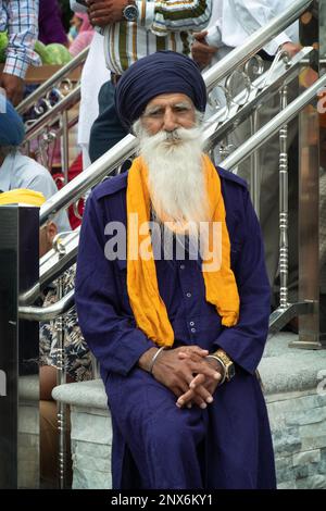 Un anziano sikh vestito di blu siede di fronte al Centro Culturale Sikh a Richmond Hills, Queens. Prima dell'inizio della parata di Nagar Kirtan Foto Stock