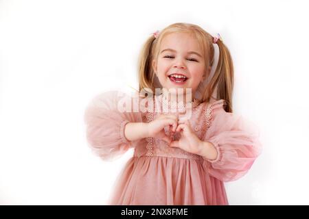 Ritratto carina ragazza felice in abito rosa su sfondo bianco risate, mostra il cuore con le dita Foto Stock