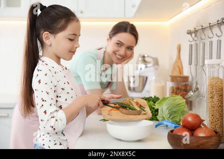Madre e figlia che pelano le verdure al bancone della cucina Foto Stock
