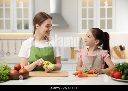 Madre e figlia che pelano le verdure al tavolo in cucina Foto Stock