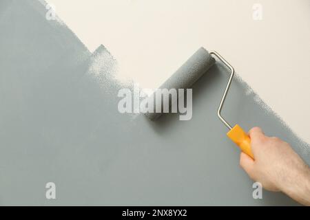 Uomo che applica vernice grigia con pennello a rullo su parete bianca, primo piano Foto Stock