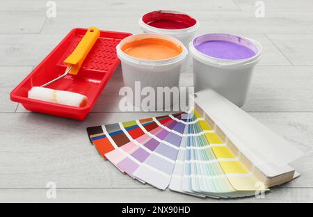 Secchi di vernici, palette e utensili decoratori su sfondo di legno chiaro Foto Stock