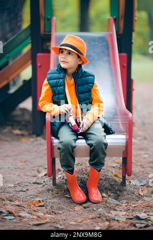 Ritratto di un ragazzo carino con un cappello arancione sul parco giochi. Foto Stock