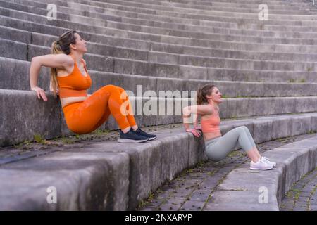 Due giovani donne caucasiche atleti in abbigliamento sportivo facendo tricep tuffi esercizio di routine su una scala Foto Stock