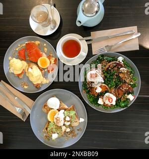 Vista dall'alto di piatti di brunch assortiti con uova, salmone, avocado, insalata, caffè e tè Foto Stock