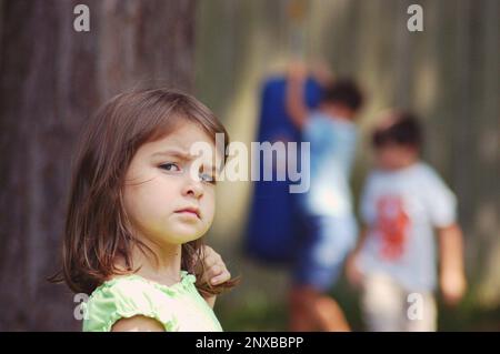 Ritratto di una ragazza infelice che si sentiva lasciata fuori con due ragazzi che giocavano sullo sfondo, USA Foto Stock